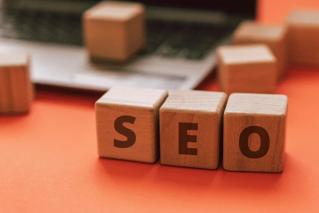 Wooden blocks spelling out "SEO" placed in front of a laptop on an orange background.